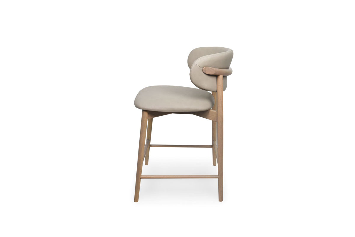 A modern counter stool with a light beige upholstered seat and curved backrest, supported by a natural wood frame with integrated armrests and slim legs.