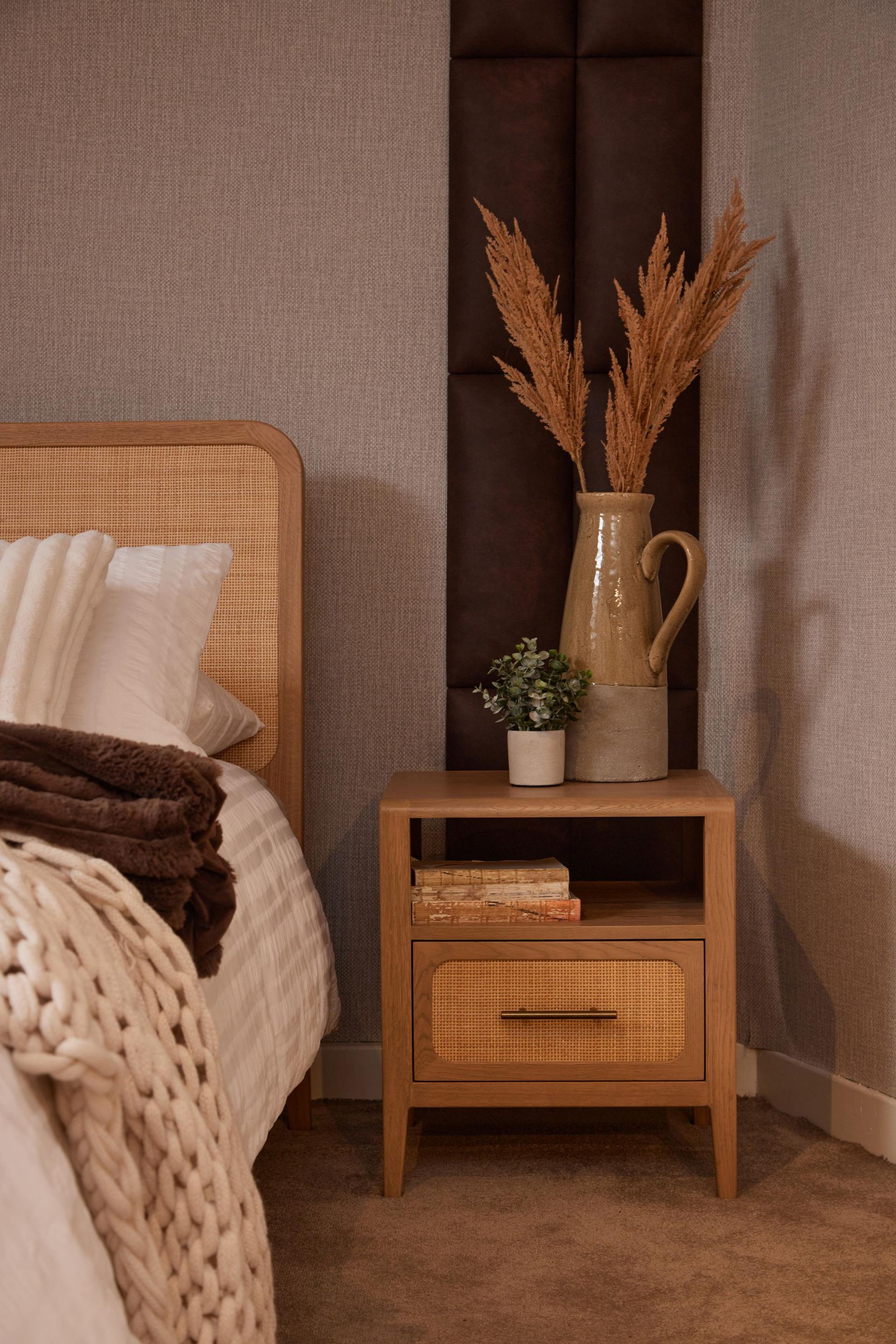Felton Bedside Locker in American oak and natural rattan with brass pull, styled with a jug of dried grasses.