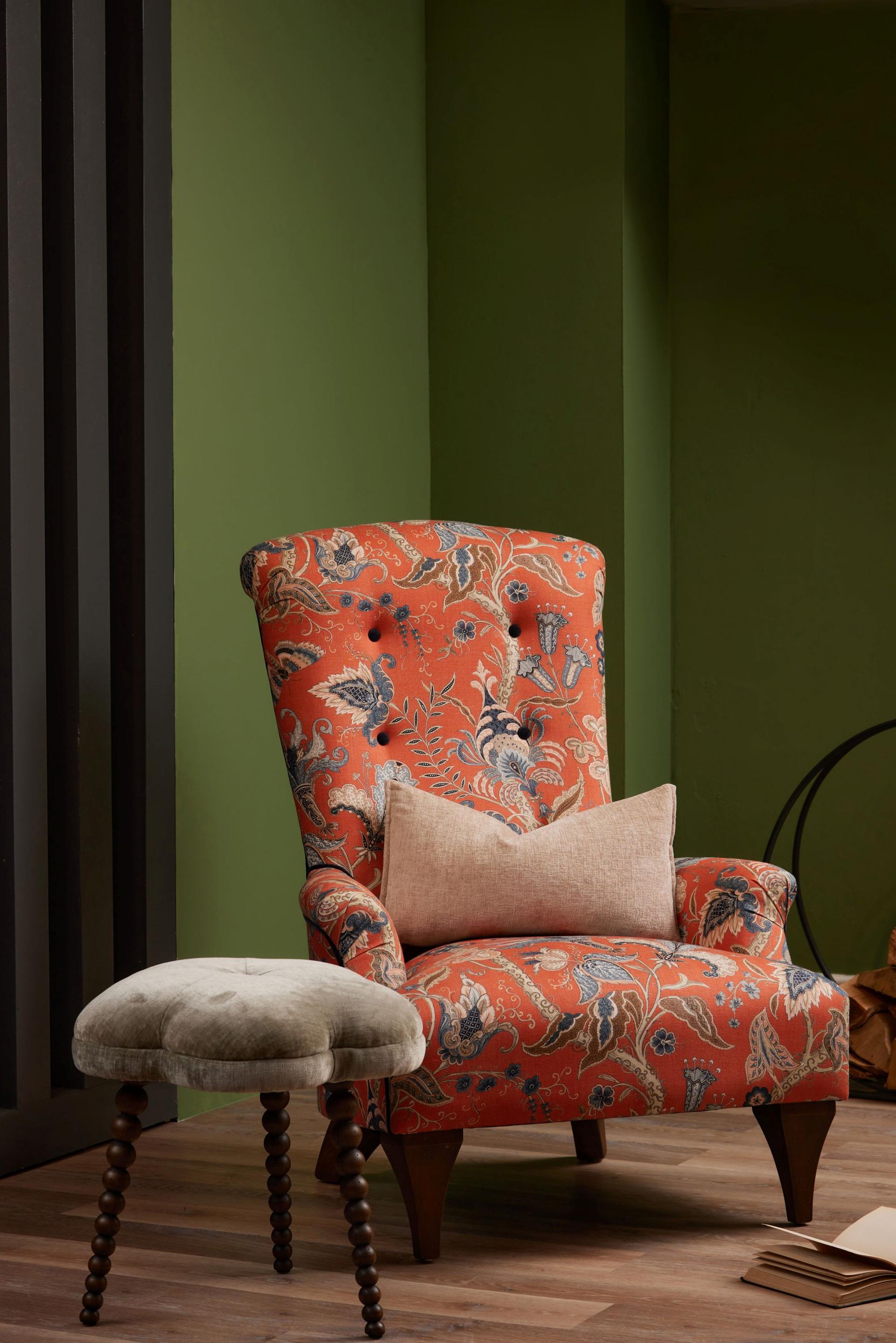 Hawthorne Armchair upholstered in vibrant Uhura Tomato floral fabric, featuring a high back and a sage green footstool with bobbin legs.