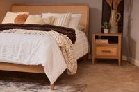 American oak Felton Bed Frame with handwoven rattan headboard, dressed in white/beige linen, beside a matching nightstand.