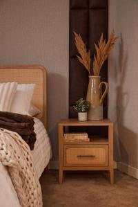 Felton Bedside Locker in American oak and natural rattan with brass pull, styled with a jug of dried grasses.
