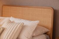 Close-up of the Felton Bed Frame's handwoven natural rattan headboard, framed by smooth American oak. White pillows visible.