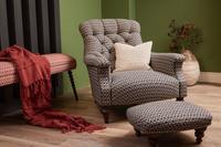 A hand-buttoned Slipper Armchair and ottoman in patterned dark fabric, Emilys Maze Midnight, with a cream pillow against a green wall.