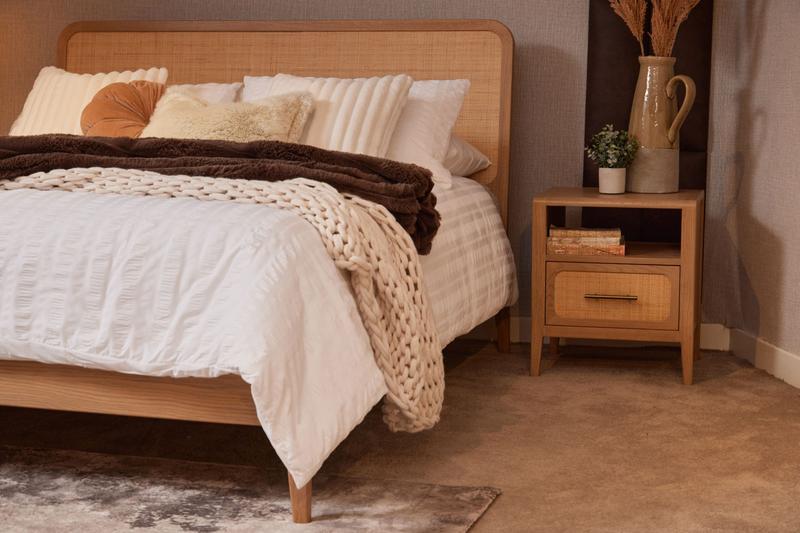 American oak Felton Bed Frame with handwoven rattan headboard, dressed in white/beige linen, beside a matching nightstand.