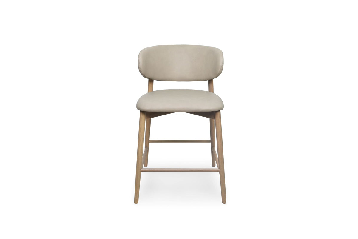 A modern bar stool with a light beige upholstered seat and curved backrest, supported by four tapered natural wood legs and front stretchers, shown against a plain white background.