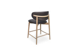 A modern bar stool with a curved chocolate upholstered backrest and seat, supported by a light natural wood frame with a curved wooden armrest and four legs, shown on a solid white background.