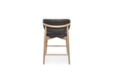 A modern bar stool with a dark chocolate upholstered seat and backrest, supported by a light natural wood frame and legs, shown from the front on a white background.