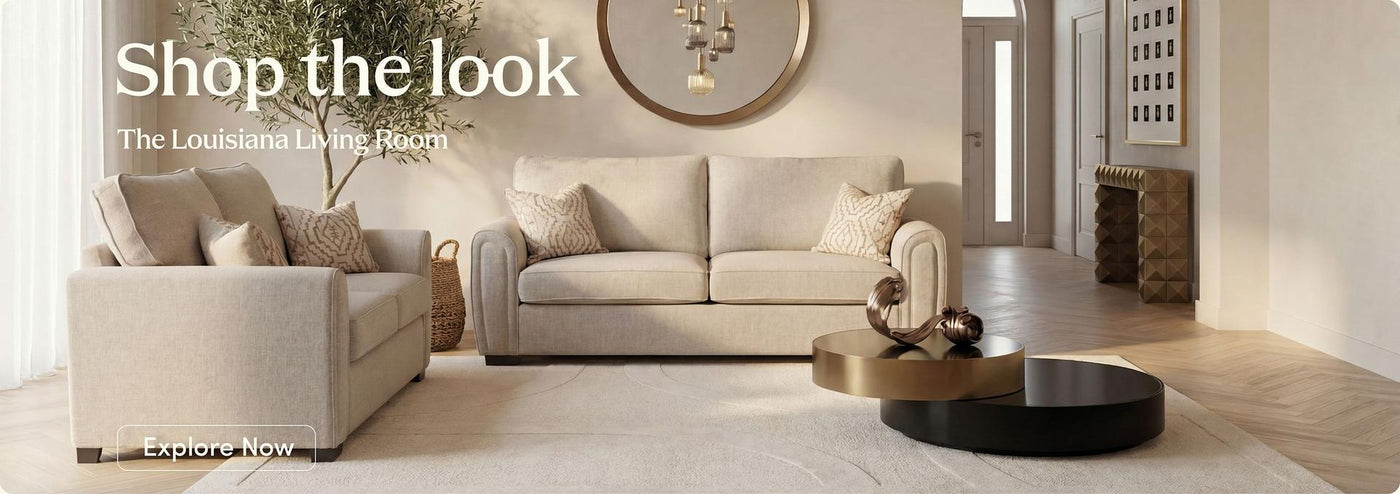 A styled living room scene featuring a light beige upholstered loveseat and a matching three-seat sofa, with decorative pillows, a round coffee table, and warm neutral decor in a bright interior.